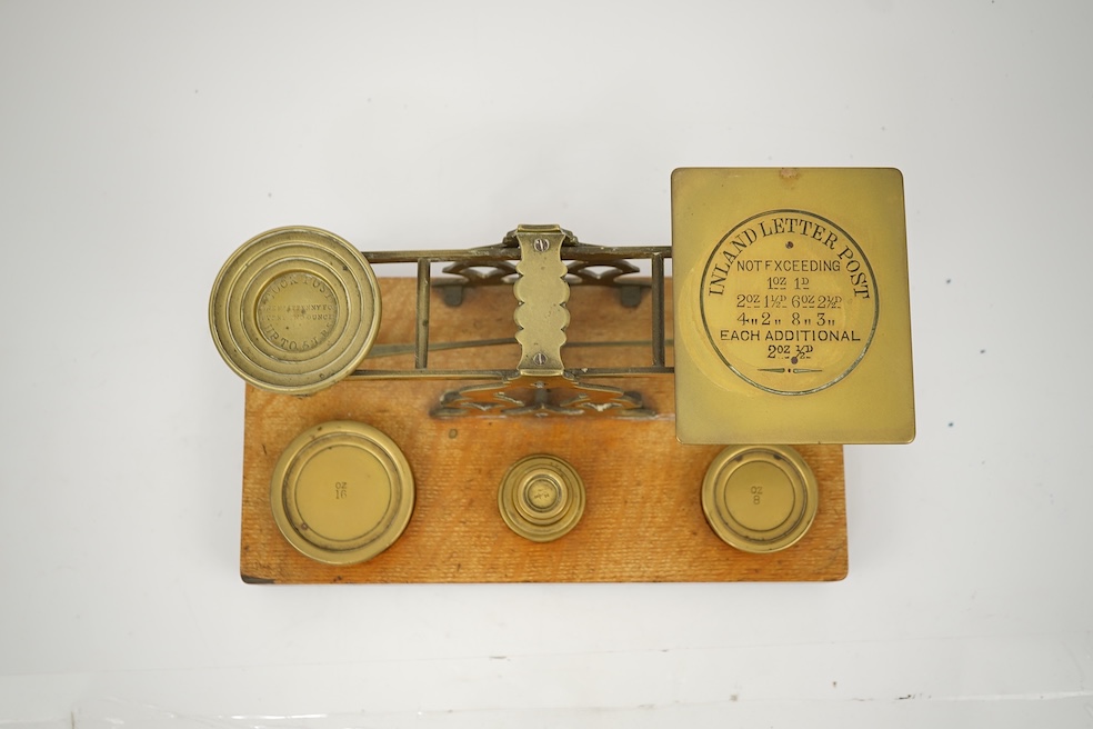 A Sampson Mordan & Co. set of brass postal scales on an oak base with weights, 27cm wide, with engraved prices for Inland Letter Post, etc.